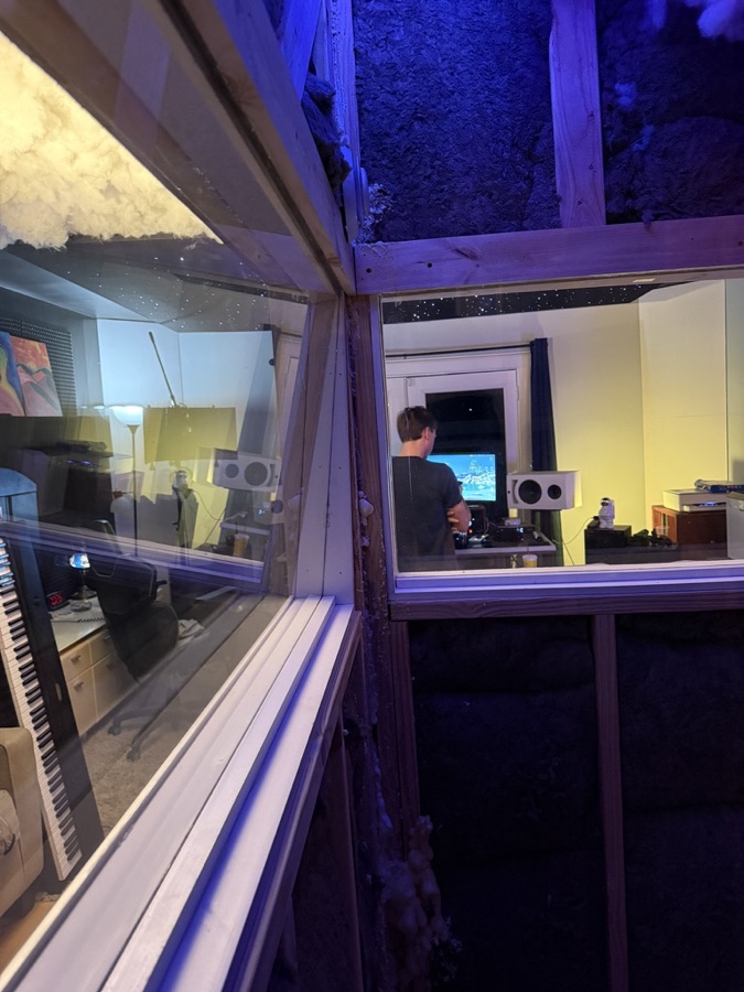 The view from inside the vocal booth, looking out through the glass at the engineer at the desk.